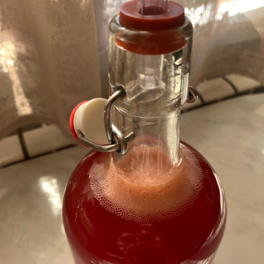 Bottle of raspberry soda with ginger bug starter culture during the process of fermentation. There are bubbles on top of the drink.